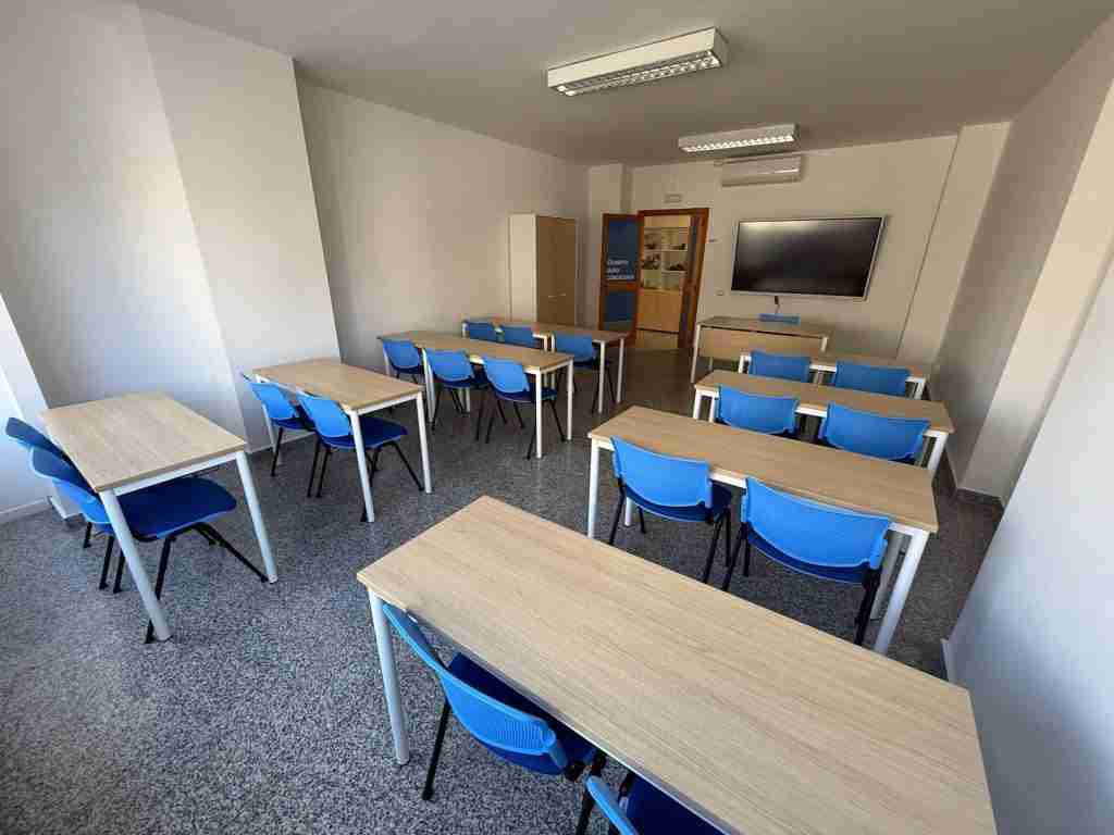 Aula moderna con scrivanie e sedie blu, attrezzata per corsi di formazione.